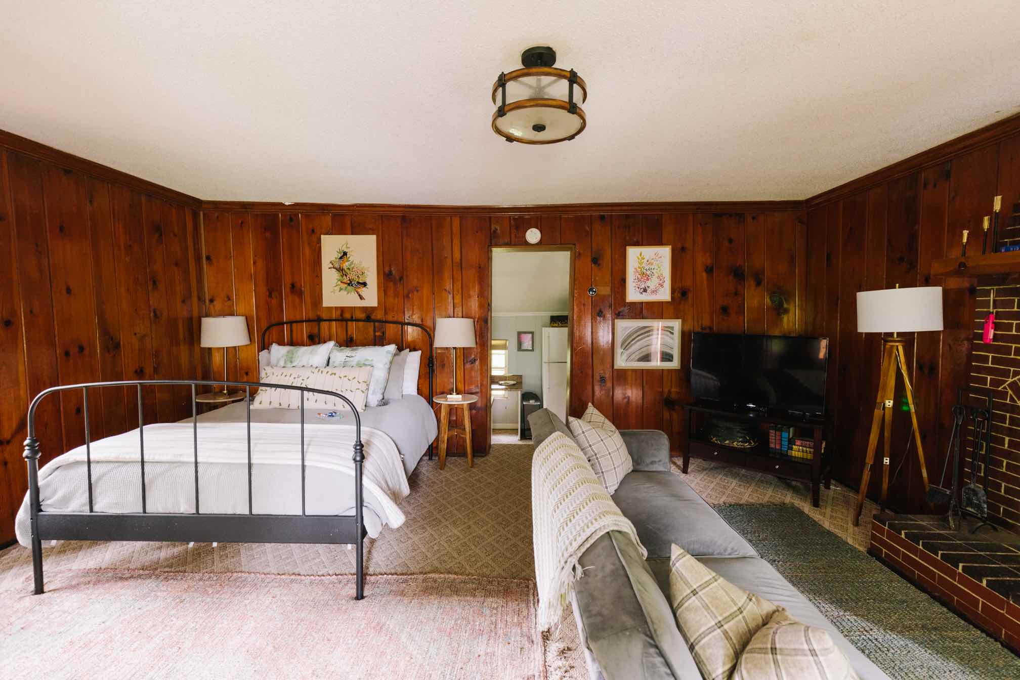 Cabin bedroom with iron bed, knotty pine walls, sofa, and brick fireplace