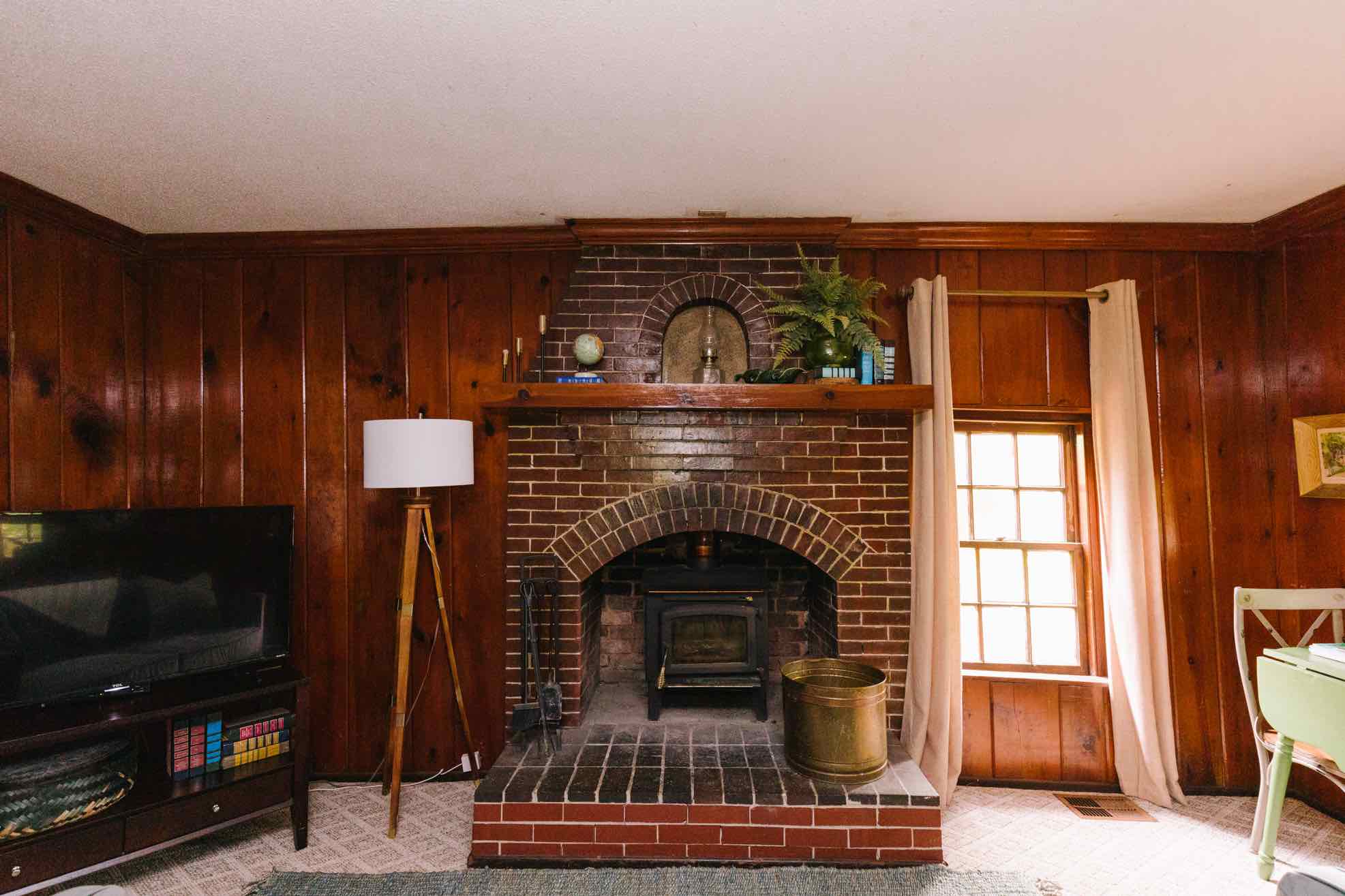 Cabin brick fireplace with wood-burning stove and warm pine paneling