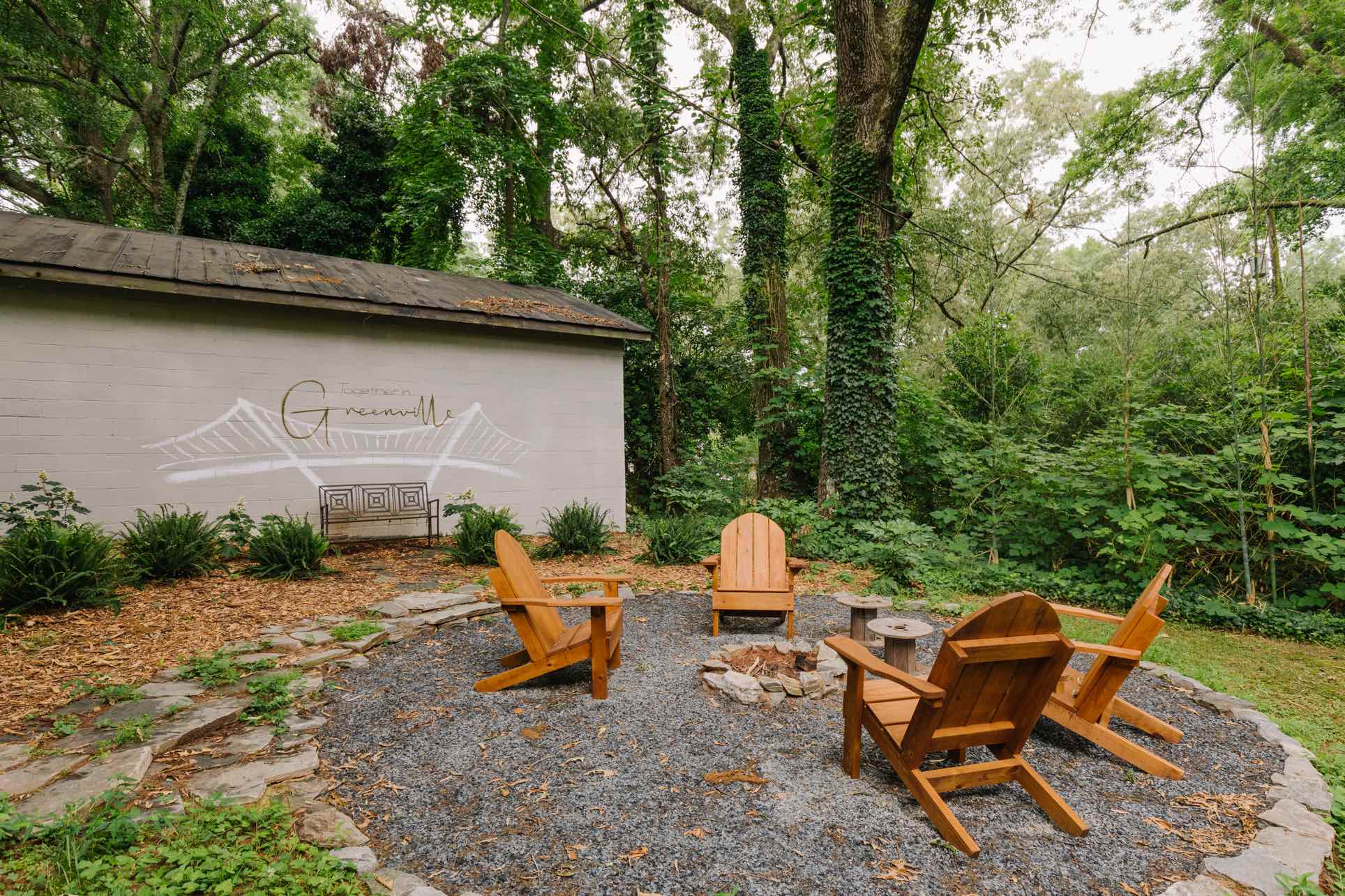 The Cabin Greenville fire pit area with Adirondack chairs and Together in Greenville mural